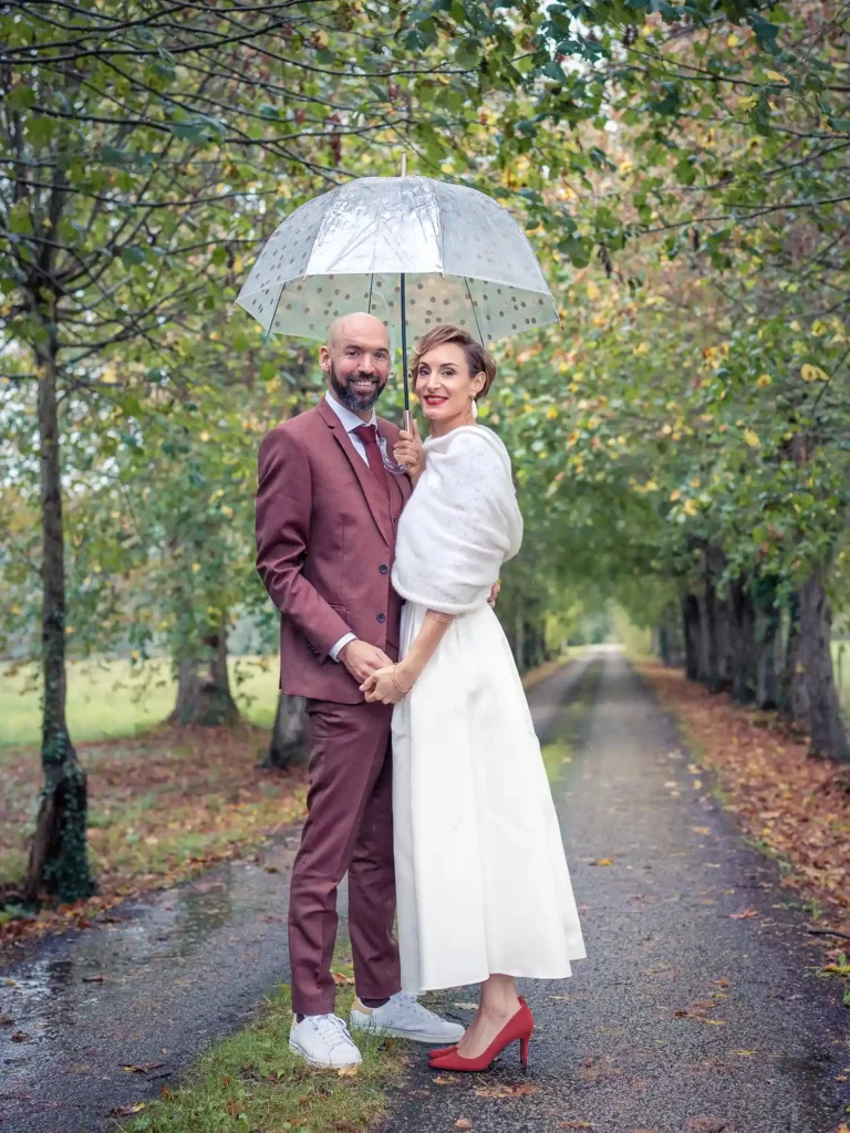 Photo de couple marié sous un parapluie dans une allée bordée d'arbres
