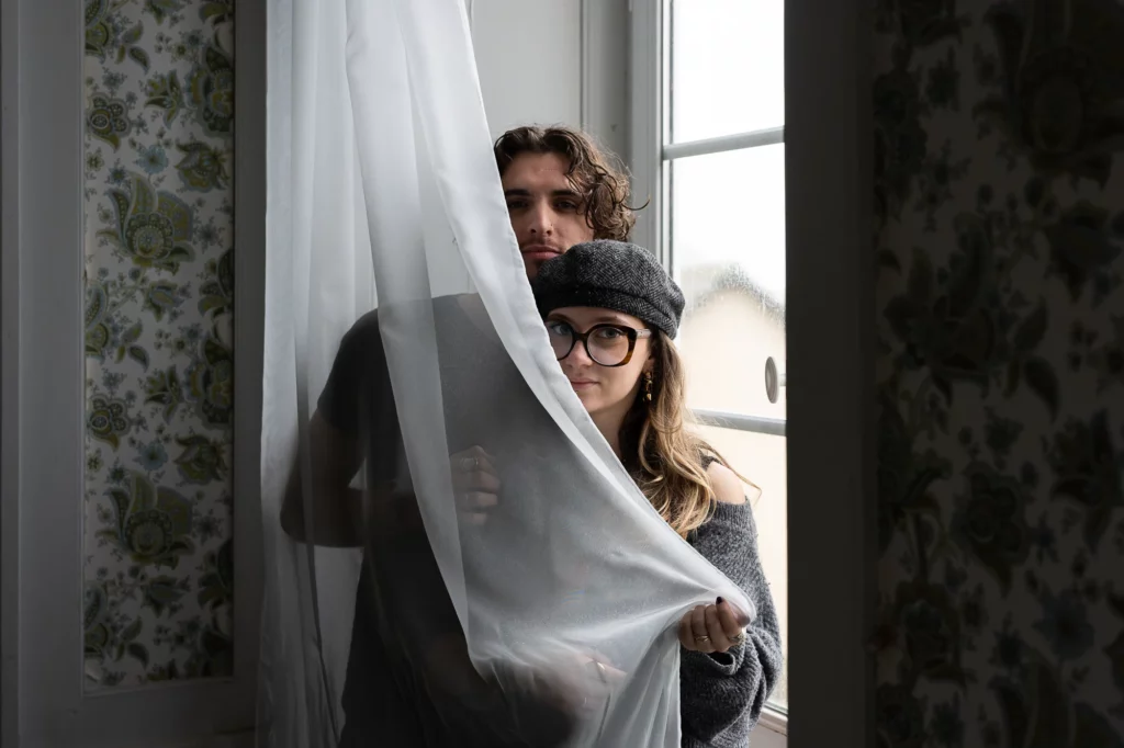 Photo de couple à la fenêtre derrière un voile.